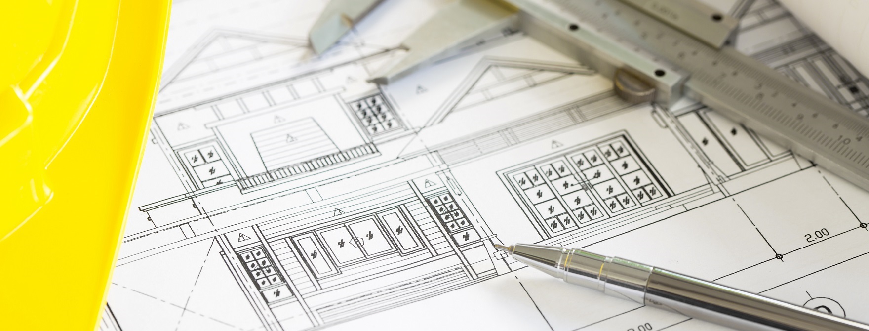 Construction plans with yellow helmet and drawing tools on blueprints